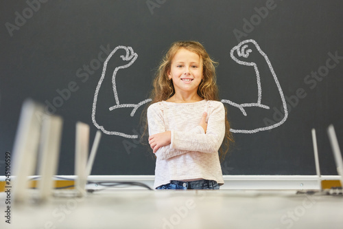 Mädchen in Schule steht vor Tafel mit Muskeln