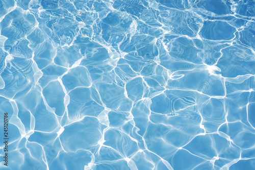 Blue water surface with bright sun light reflections, water in swimming pool background