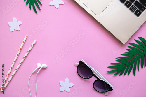 Workspace in a pink trendy color or summer design with a concept to start a vacation. Laptop and sunglasses next to tropical leaves. Nearby there is a place for text.