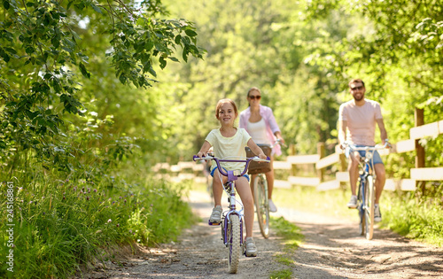 family, leisure and people concept - happy mother, father and little daughter riding bicycles in summer park