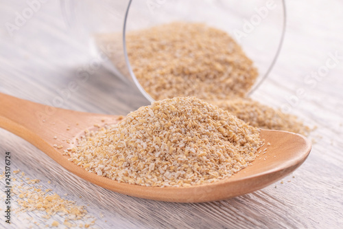 Oat bran in a wooden spoon and in a glass transparent glass on a white wooden table