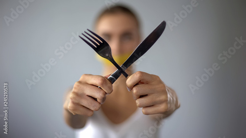 Woman crossing fork and knife, mouth closed with tape, self-restriction in food