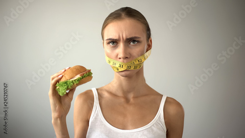 Slim girl with taped mouth fights with temptation to eat burger, dieting