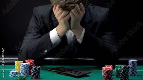 Young devastated businessman losing poker game at casino, gambling addiction