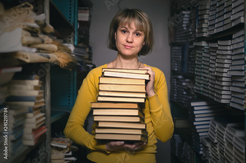 Skeptical librarian holding in hands a stack of books in the library. Exam preparation.