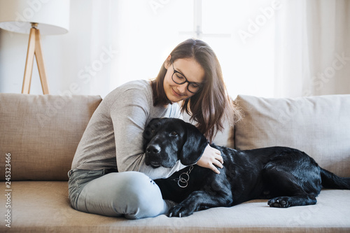 Teenage girl sitting on a sofa indoors, playing with a pet dog.