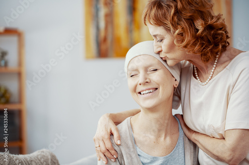 Senior redhead woman kissing forehead of her happy best friend suffering from cervical cancer
