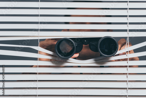 suspicious young man with binoculars spying through blinds