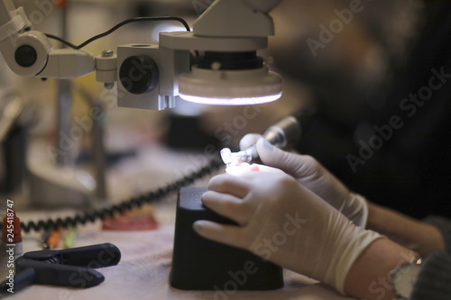 The hands of a dental technician processing a prosthesis with a drill under the microscope