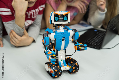 Group of kids building robot constructor from the plastics details programmed on the computer, at robotics school lesson. Education, children, technology, science and futuristic concept. E-learning. 