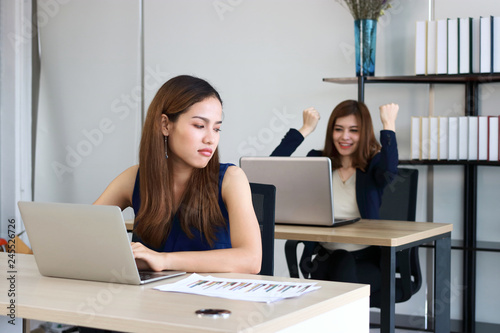 Young angry envious Asian business woman looking successful competitor colleague in office.