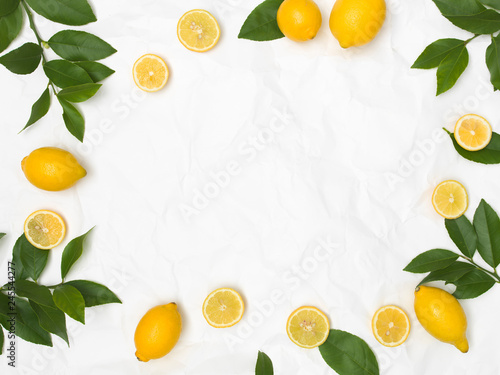 many fresh lemons and green leaves on white crumpled paper background