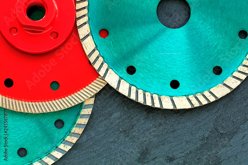 Several diamond cutting wheels of red and emerald color against a background of gray granite.