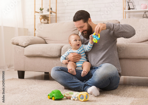 Happy father playing with his baby son with bright rattle