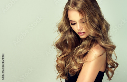 blondynka z długimi i lśniącymi falującymi włosami. Piękny uśmiechnięty kobieta model z kędzierzawą fryzurą.