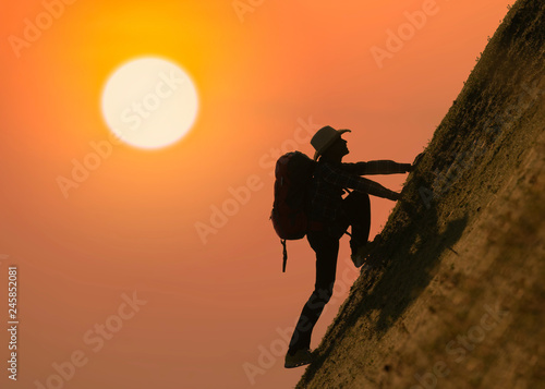 Silhouette of backpacker climbing on mountain at sunset or sunrise