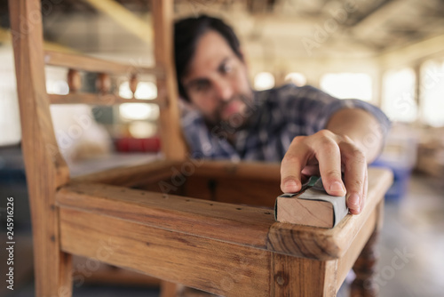 Skilled woodworker sanding a chair in his workshop