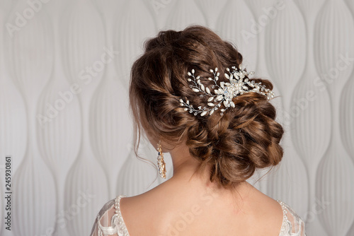 Wedding female hairstyle low beam on the head of a brown-haired girl back view on a light background.
