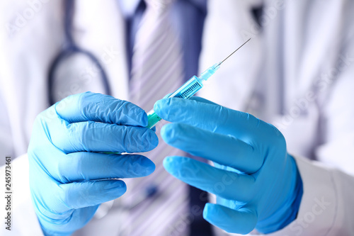 Physician arms wearing protective blue gloves prepare syringe