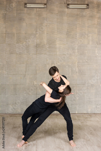 Young couple performing romantic dance. Boy gently holding his dancing partner over grey background. Skillful boy and girl practicing sensual dance.