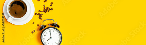 Flat lay cup of black coffee, coffee beans, black alarm clock on yellow background top view copy space. Minimalistic food concept, morning breakfast, time to work, hot drink, coffee background