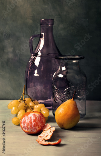 Still life with blue glass vase, lilac glass jar and fruit on turquoise background