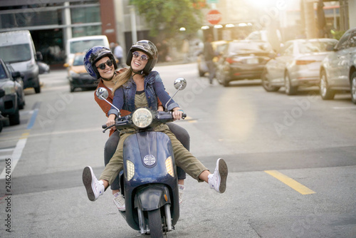 Happy young women riding scooter together in city