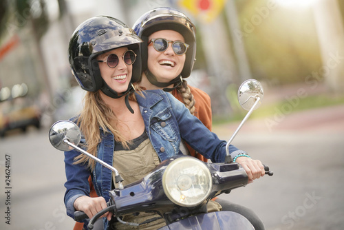 Happy young women riding scooter together in city