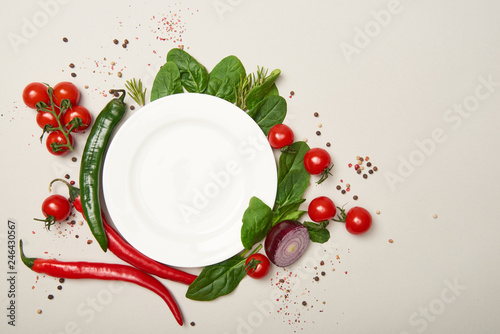 Top view of white plate, vegetables and spices on grey background