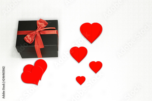 Czarne pudełko z czerwoną wstążką i sercami na białym tle.