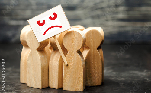 An angry mob of wooden figures of people with a poster. Social discontent and social tension, protest and disagreement. People go outside and join the protest movement. Disobedience and disobedience.