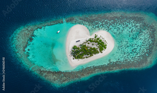 Drone Aerial view of beautiful tropical heart shaped island among blue sea water at Maldives paradise with boat on background