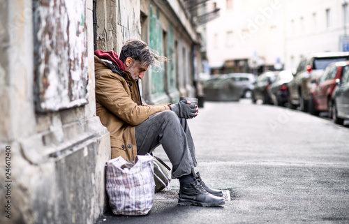 Homeless beggar man sitting outdoors in city asking for money donation.