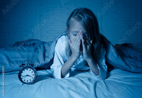 Little girl suffering from insomnia looking at alarm clock feeling desperate sad and restless