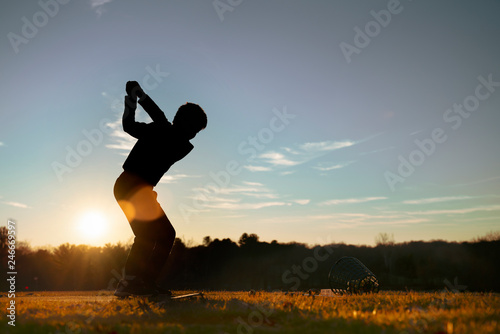 Young junior golfer practicing in a driving range with beautiful sunset light in winter.