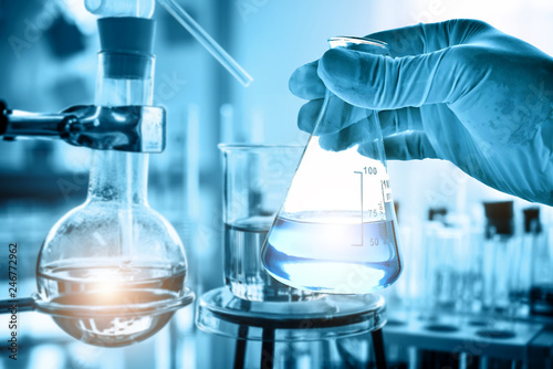 hand of scientist holding flask with lab glassware in chemical laboratory background, science laboratory research and development concept 