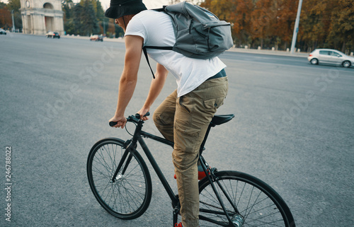 Young modern man cycling on a classic bike on the city road with a backpack