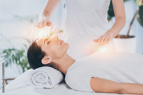 side view of calm young woman receiving reiki healing therapy on head and chest