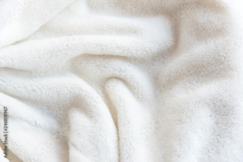 White delicate soft background of plush fabric. Texture of beige soft fleecy blanket textile with twisted folds.