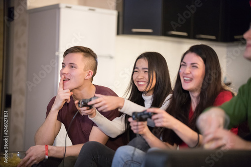 Company of young friends spending time together. Two young woman playing game using a joystick. Excitement