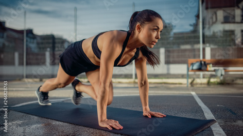 Beautiful Energetic Fitness Girl Doing Mountain Climber Exercises. She is Doing a Workout in a Fenced Outdoor Basketball Court. Evening After Rain in a Residential Neighborhood Area.