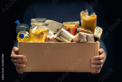 A man holding a donation box of different products on dark background