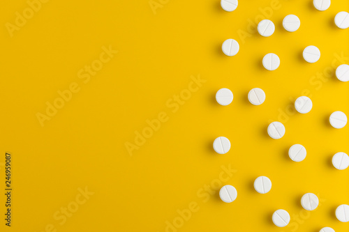 White medication pills arrangement on yellow background. Flat lay. Copy space.