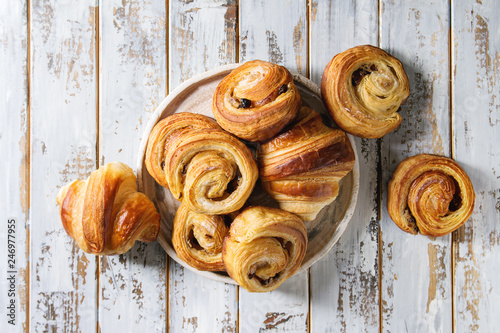 Variety of homemade puff pastry buns cinnamon rolls and croissant in ceramic plate over white plank wooden background. Flat lay, space