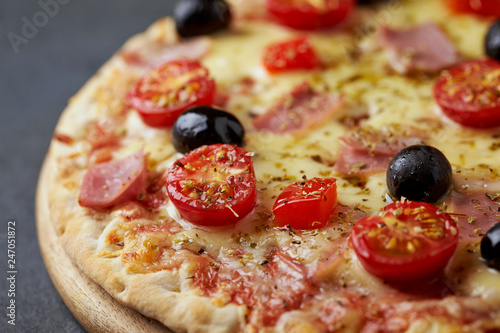 Pizza with ham, mozzarella cheese, cherry tomatoes, red pepper, black olives and oregano. Home made food. Concept for a tasty and hearty meal. Black stone background. Copy space