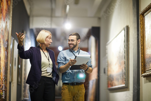 Portrait of two cheerful museum workers discussing paintings walking in art gallery, copy space