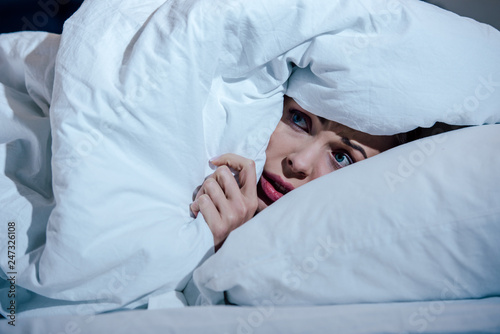 scared woman hiding behind blanket in bedroom at home