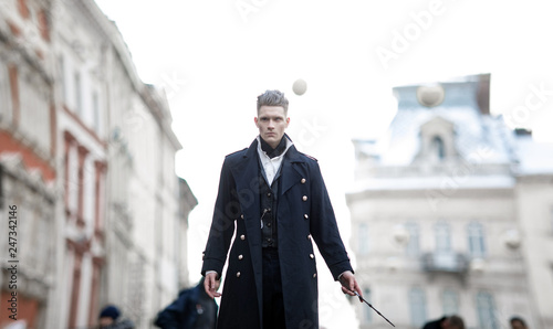 Young man in image of black magician walks on street with magic wand.
