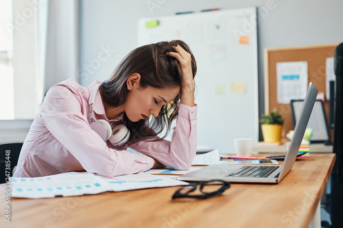 Young woman with headache sitting in office holding head