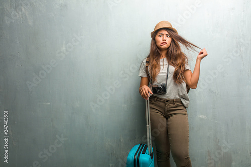 Portrait of young traveler latin woman against a wall crazy and desperate, screaming out of control, funny lunatic expressing freedom and wild. Holding a blue suitcase.